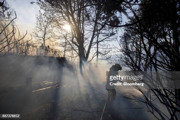 Firefighter hoses down the perimeter of a partially burned home during the Skirball Fire in the Bel Air neighborhood of Los Angeles, California,...