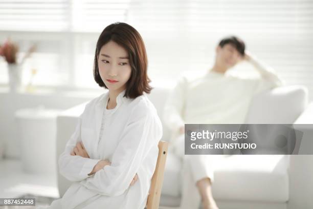 woman with angry expression, man in background - stressed young woman sitting on couch stock-fotos und bilder