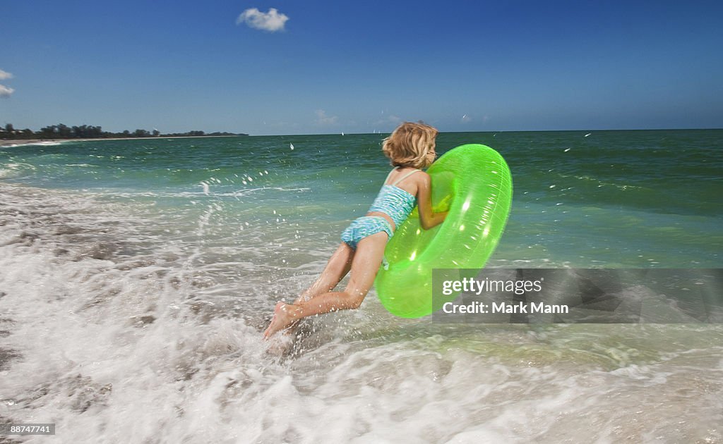 Young girl jumping with innertube at the beach.