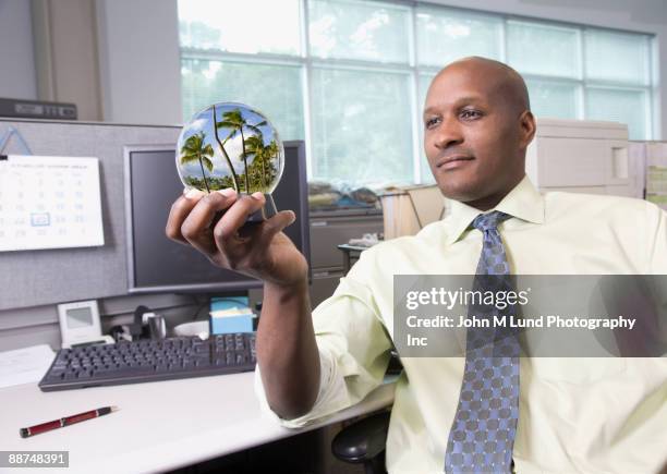 african businessman viewing vacation in snow globe - snow globe stock-fotos und bilder