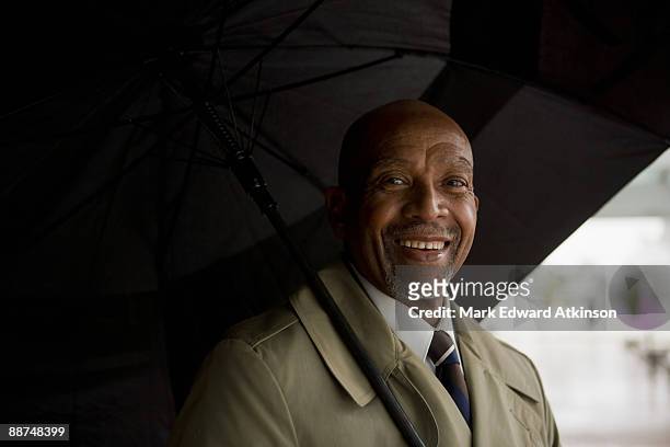 african businessman holding umbrella - trench coat stockfoto's en -beelden