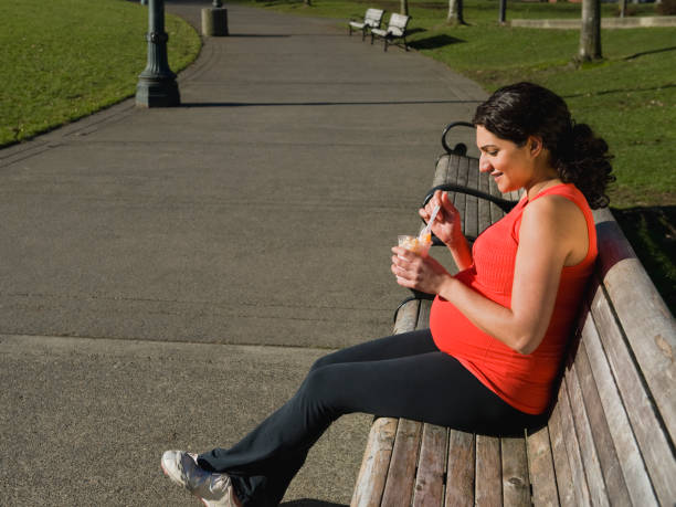 pregnant middle eastern woman eating fruit in park - eat before or after workout stock pictures, royalty-free photos & images