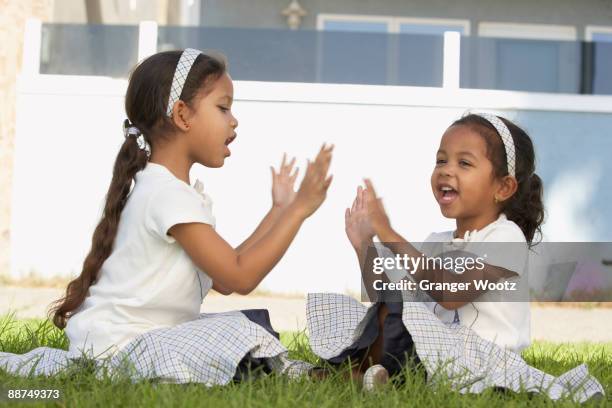 young mixed race girls sitting and playing pat-a-cake - chanten stockfoto's en -beelden