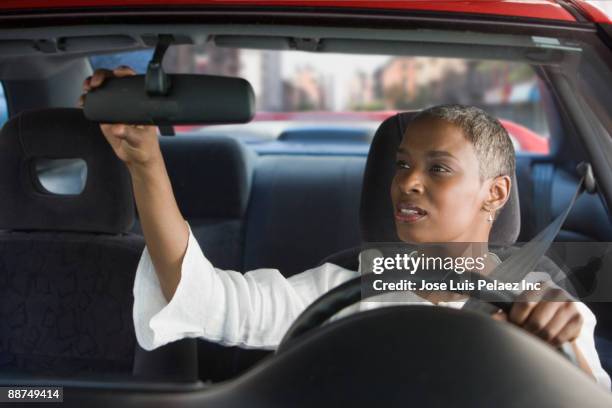 african woman in car adjusting mirror - vehicle mirror stock-fotos und bilder