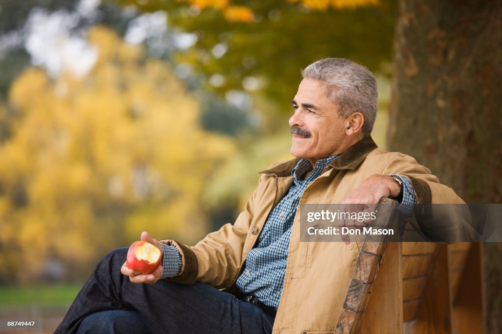 African man eating apple on park bench