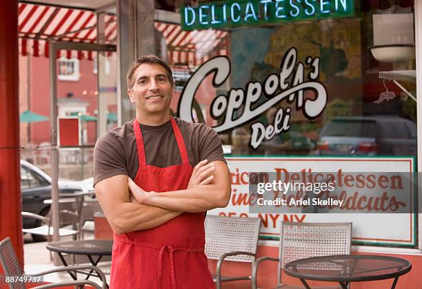 mixed race business owner in apron in front of deli - store sign stockfoto's en -beelden