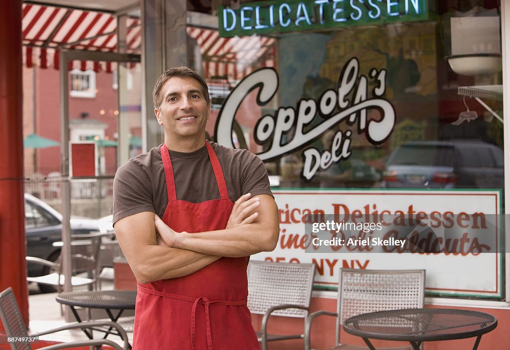 Mixed race business owner in apron in front of deli