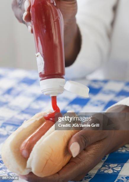 african woman putting ketchup on hot dog - squirt stockfoto's en -beelden