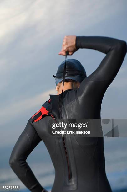 hispanic woman zipping wetsuit on beach - wetsuit stock pictures, royalty-free photos & images