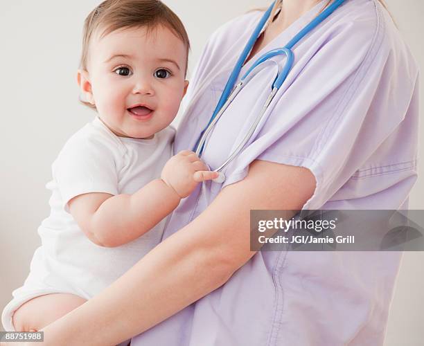 nurse holding mixed race baby girl - nurse and portrait and white background and smiling and female and looking at camera stock pictures, royalty-free photos & images