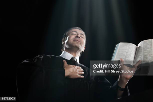 hispanic priest holding bible with eyes closed - geestelijken stockfoto's en -beelden