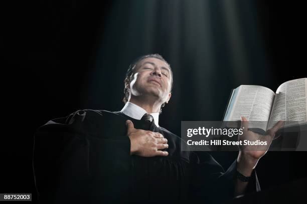 hispanic priest holding bible with eyes closed - clergy stock pictures, royalty-free photos & images