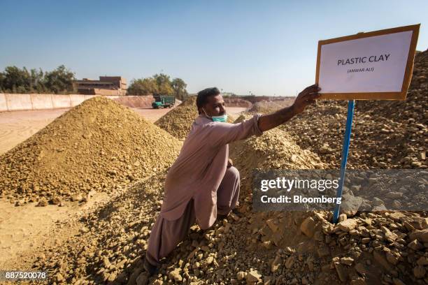 Worker reaches for a sign standing in a pile of clay in a preparation unit at the Shabbir Tiles & Ceramics Ltd. Production facility in Karachi,...