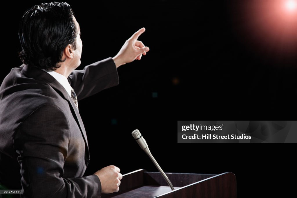 Hispanic man at podium with arm raised