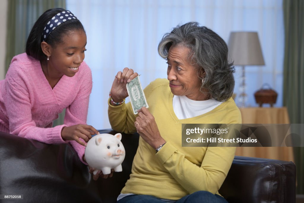 African woman giving granddaughter dollar bill for piggy bank
