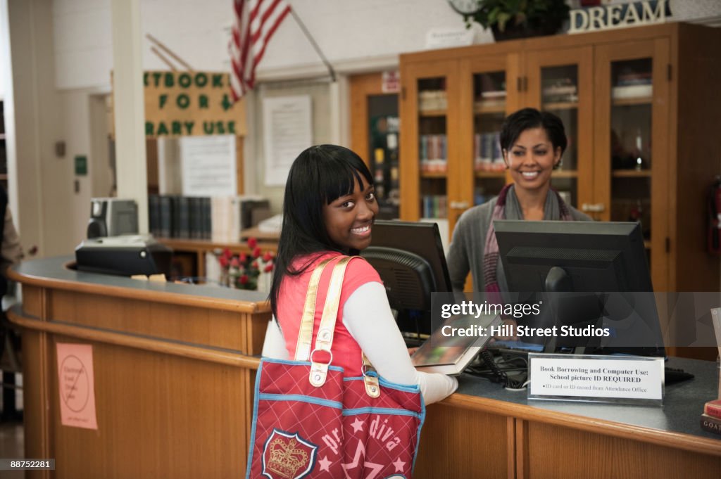 African teenage girl checking out book from school library