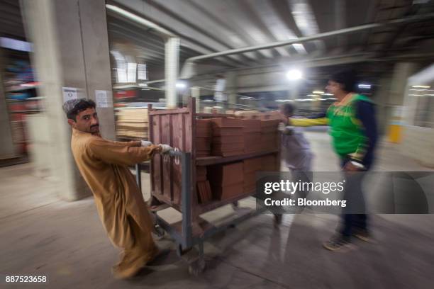 Employees move a cart laden with unglazed tiles at the Shabbir Tiles & Ceramics Ltd. Production facility in Karachi, Pakistan, on Wednesday, Dec. 6,...