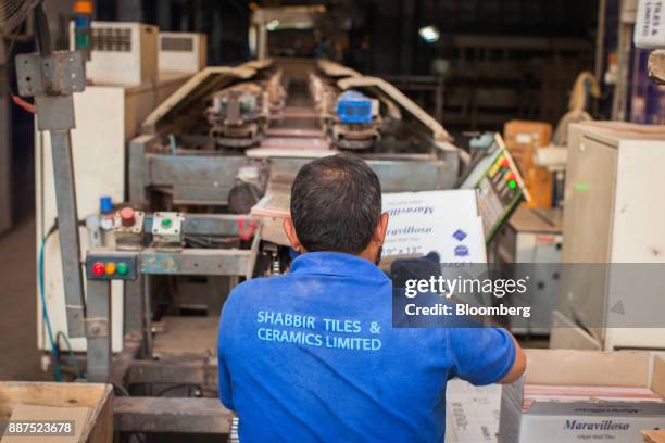 An employee packs tiles from a conveyor into a box at the Shabbir Tiles & Ceramics Ltd. Production facility in Karachi, Pakistan, on Wednesday, Dec....