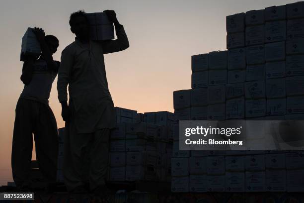 The silhouettes of workers are seen as they load boxes of tiles onto a truck at the Shabbir Tiles & Ceramics Ltd. Production facility at dusk in...