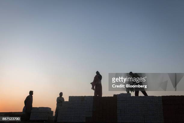 The silhouettes of workers are seen as they stand on boxes of tiles stacked on trucks at the Shabbir Tiles & Ceramics Ltd. Production facility at...