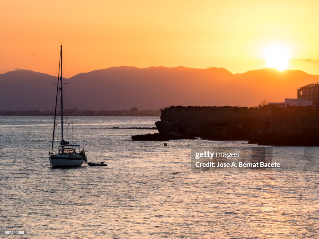 Silhouette of a sailboat in the sea near a harbor, during a sunset between the mountains on the island of Tabarca