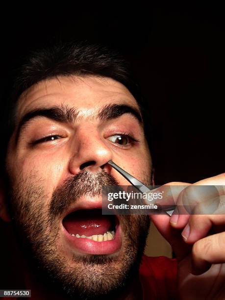 man plucking nasal hair with tweezers - male hair removal stockfoto's en -beelden