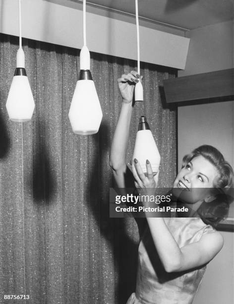 Young woman fitting the latest in light bulbs from General Electric, the 'Celeste', circa 1955.