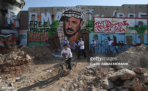 Group of Palestinian youths cycle past a section of Israel�s separation barrier to promote a cultural festival in the West Bank city of Ramallah and...