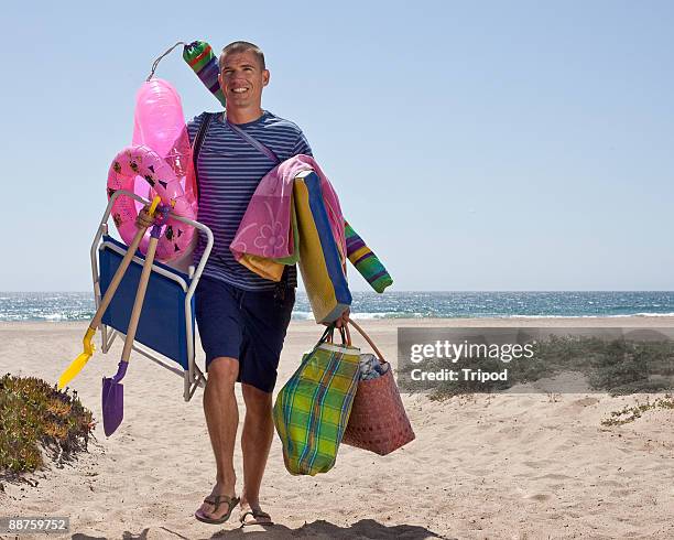 man carrying bags, chairs, shovels at beach - hombres de mediana edad fotografías e imágenes de stock