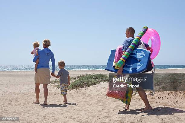 mother with children on beach, father behind - carrying fotografías e imágenes de stock