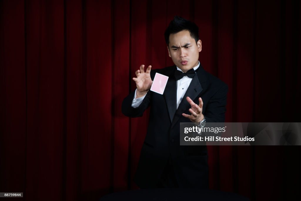 Asian magician in tuxedo doing magic trick onstage