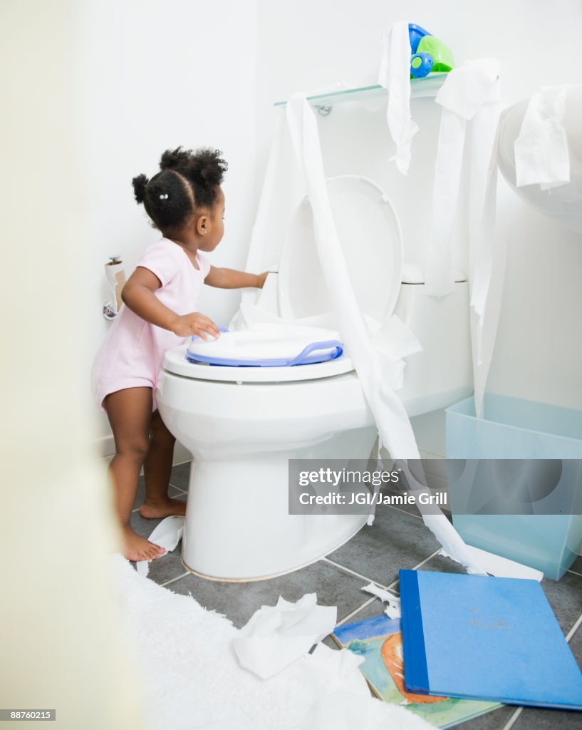 African American girl spreading toilet paper around bathroom