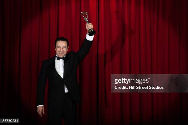hispanic man in tuxedo holding trophy onstage - preisverleihung stock-fotos und bilder