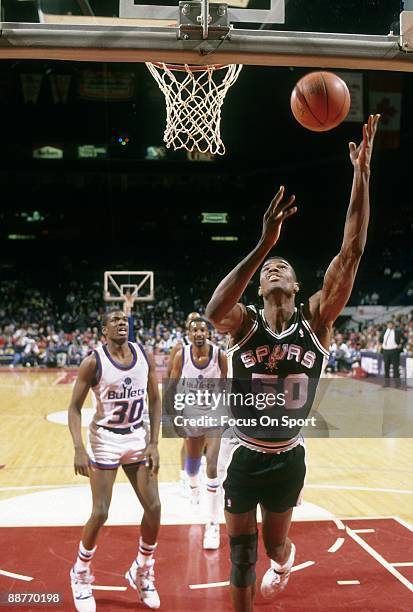 S: David Robinson of the San Antonio Spurs lays the ball up in front of Bernard King and Charles Jones of the Washington Bullets during an early...