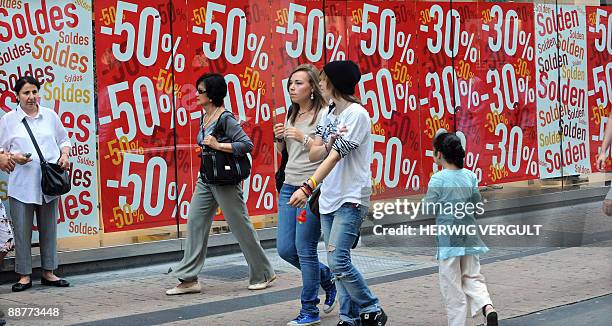 People walk past a large window with posters reading announcing price reductions, at the start of the summer sales period, in the 'Nieuwstraat - Rue...