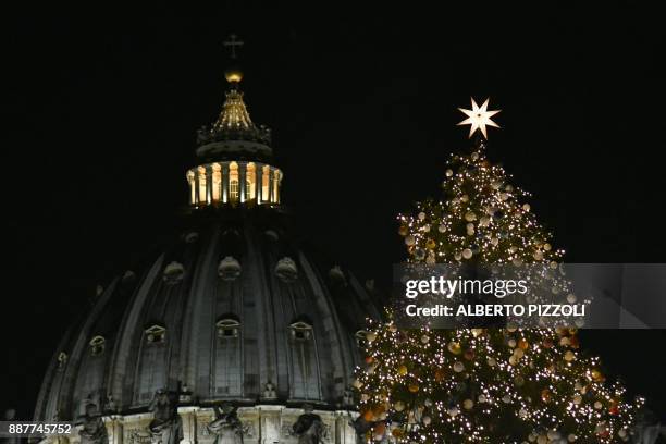 The christmas tree of St Peter's square is illuminated with the dome of St Peter's basilica in the background during the inauguration of the...