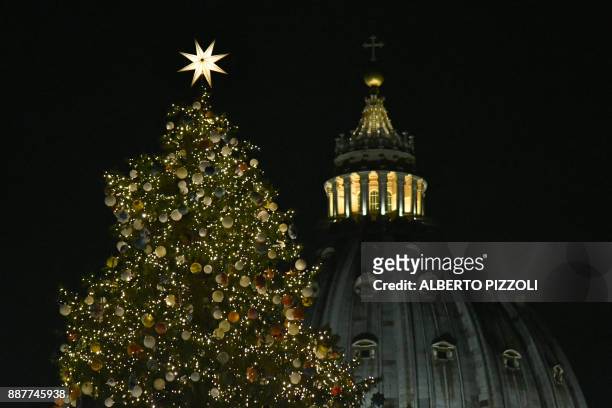 The christmas tree of St Peter's square is illuminated with the dome of St Peter's basilica in the background during the inauguration of the...