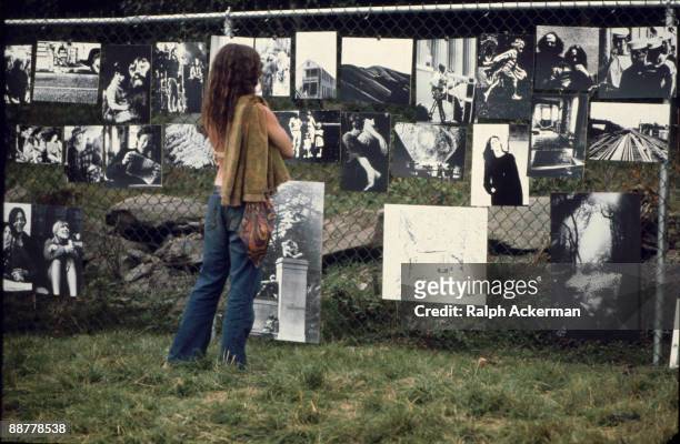 Female festival goer looks at a gallery of photographs hanging upon a chain link fence and exhibited at the Woodstock Music Festival, Bethel, NY,...