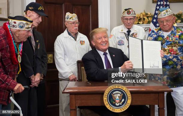 President Donald Trump, surrounded by Pearl Harbor survivors, holds up a proclamation after signing during an event marking National Pearl Harbor...