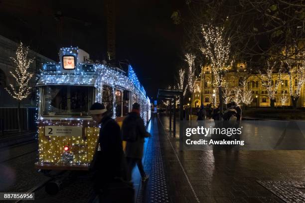 Two passer by walk in front of the traditional special festive Christmas lit Tram n2 on December 7, 2017 in Budapest, Hungary. The traditional...