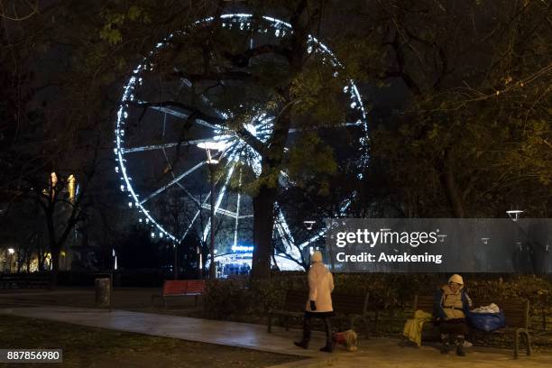 An homeless woman sits on a bench in front of the Budapest Eye on December 7, 2017 in Budapest, Hungary. The traditional Christmas market and lights...