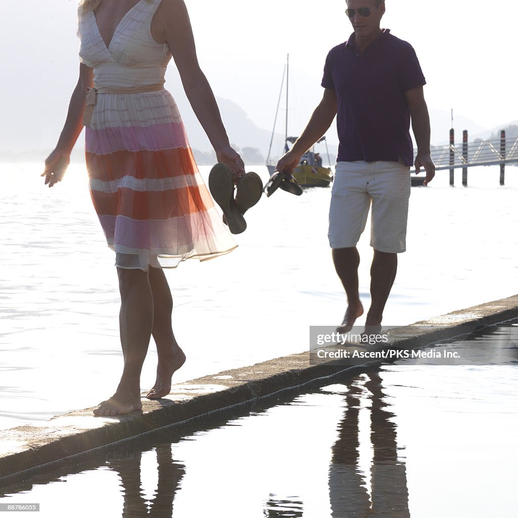 Couple walk along stone wall dividing lake