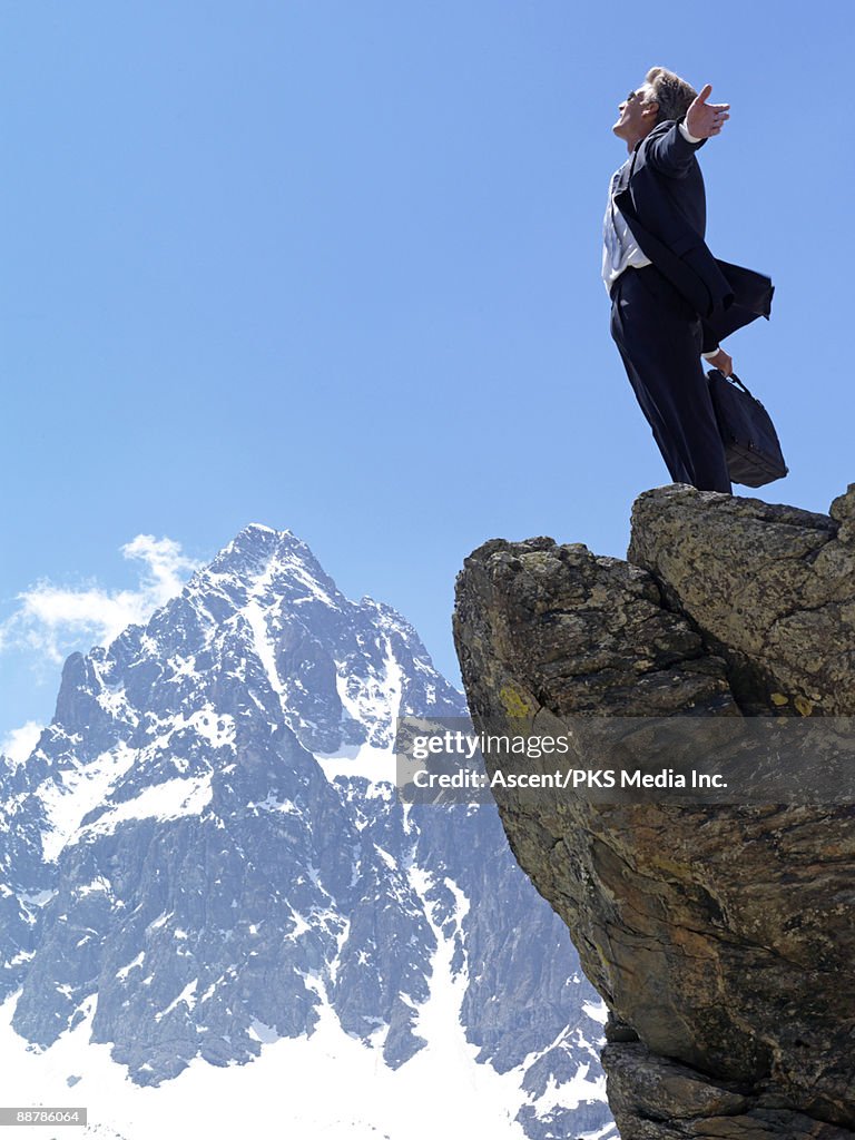Businessman stands on mountain summit, arms out