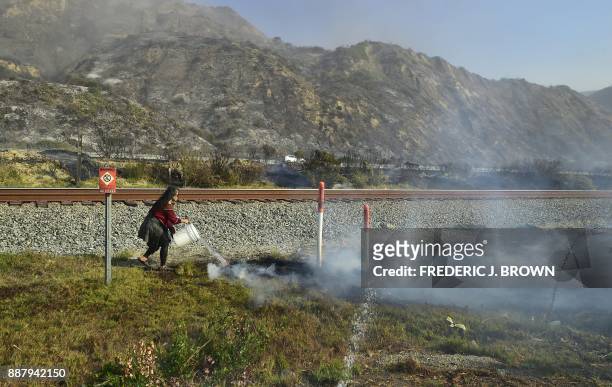 Woman helps water down burning embers across from her home beside the US 101 freeway at the beachside community of Faria Beach, northwest of Ventura,...