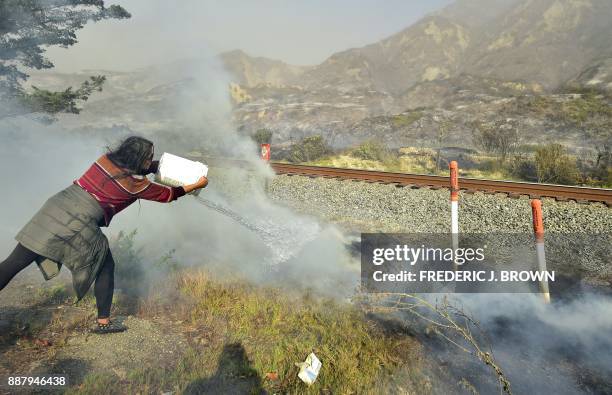 Songsri Kesonchampa tosses a bucket of water onto burning embers across the road from her home beside the US 101 freeway, southbound, in the...