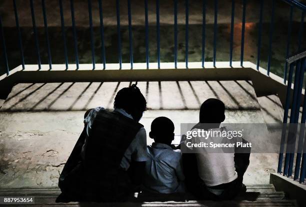 Children, displaced residents of the island of Barbuda, look at a mobile device while at a shelter at a cricket stadium on December 7, 2017 in St...