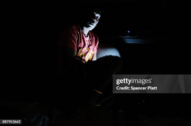 Displaced resident of the island of Barbuda looks at his mobile phone while at a shelter at a cricket stadium on December 7, 2017 in St John's,...