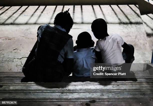 Children, displaced residents of the island of Barbuda, look at a mobile device while at a shelter at a cricket stadium on December 7, 2017 in St...