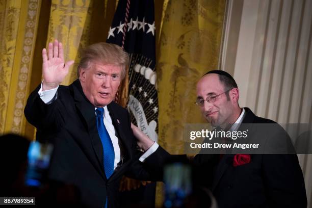 President Donald Trump waves as Rabbi Meir Soloveichik looks on during a Hanukkah Reception in the East Room of the White House, December 7, 2017 in...