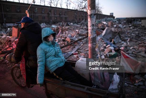 Chinese girl rides in the back of a scooter as it passes the rubble of buildings demolished by authorities in an area that used to have migrant...